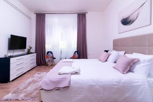 biała sypialnia z dużym białym łóżkiem z różowymi poduszkami w obiekcie Jevrejska - Central Apartment with Free Parking w Nowym Sadzie