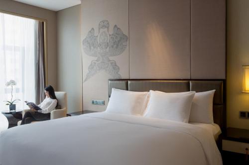 a woman sitting in a chair next to a large bed at Pullman Weifang in Weifang