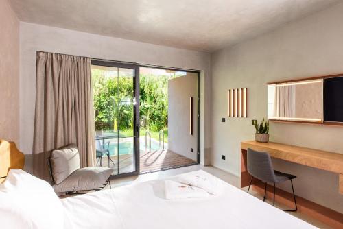 a bedroom with a bed and a desk and a balcony at Pilot Amphora Boutique Hotel "Adults Only" in Georgioupolis
