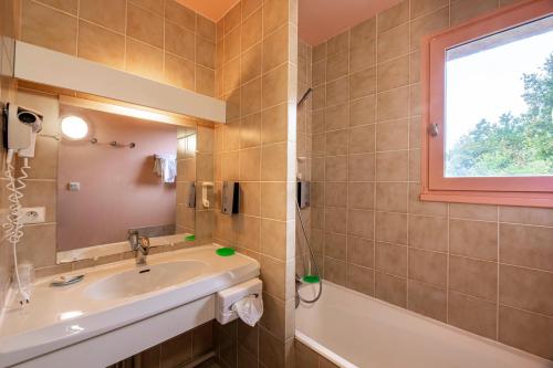 La salle de bains est pourvue d'un lavabo, d'une fenêtre et d'une baignoire. dans l'établissement Hôtel du Lac, à Lacapelle-Viescamp