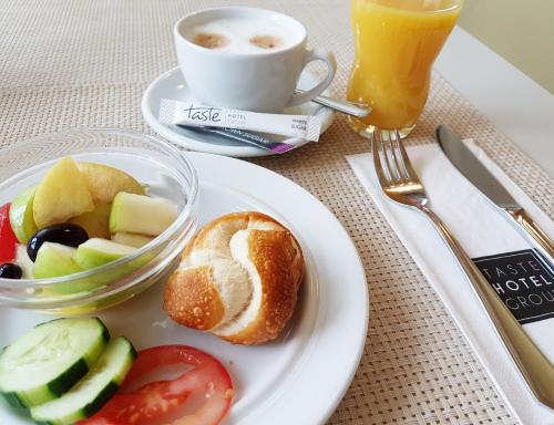 a plate of food with a bowl of fruit and a cup of coffee at Taste Hotel Hockenheim in Hockenheim