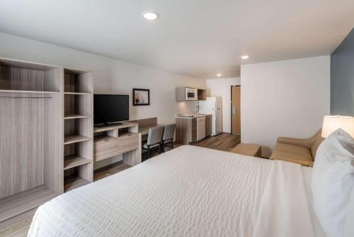 a bedroom with a white bed and a desk with a television at WoodSpring Suites Tri-Cities Richland in Richland