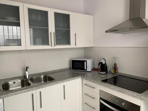 a kitchen with white cabinets and a sink and a microwave at Apartamento Mirando al Guadiana Centro in Ayamonte