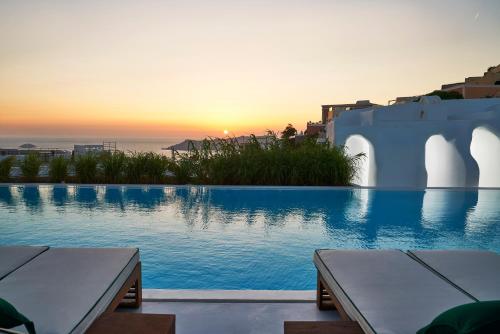 a swimming pool with a sunset in the background at Katikies Garden Santorini - The Leading Hotels Of The World in Fira