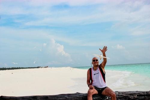 a man sitting on a beach with his hand in the air at Sabba Beach Suite , Fodhdhoo - Maldives in Velidhoo