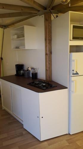 Il comprend une cuisine blanche équipée d'une cuisinière et d'un réfrigérateur. dans l'établissement Tipi Les P'tites Maisons dans la Prairie, à Sallertaine