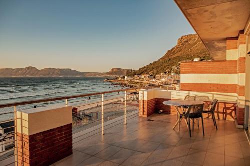 balcón con mesa, sillas y vistas al océano en Surferscorner Self Catering Apartments, en Muizenberg