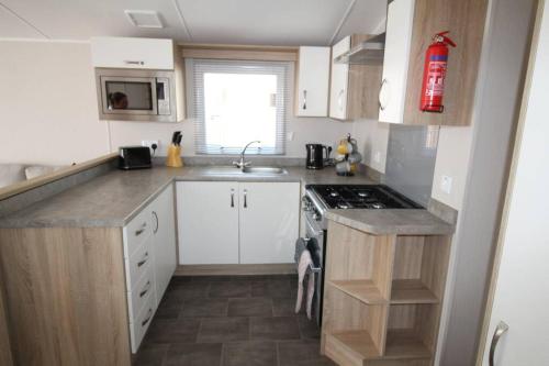 a small kitchen with white cabinets and a stove at The One - Chalet in the Cairngorms in Boat of Garten