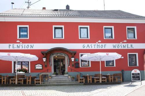 a red building with tables and umbrellas in front of it at Gasthof Wösner in Münzkirchen