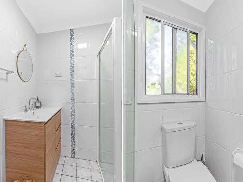 a white bathroom with a toilet and a window at Mobys at Hyams Beach in Hyams Beach