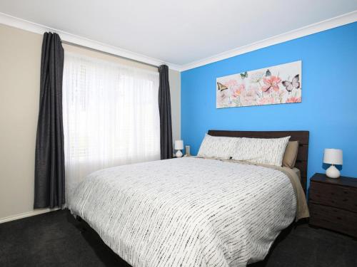 Dormitorio azul con cama y ventana en Kingfisher I Pet Friendly I 10 Min Walk to Beach en Sanctuary Point