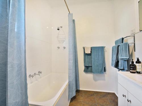 a bathroom with a tub and a shower with blue towels at Nest I Pet Friendly I 2 Min Walk to Beach in Currarong