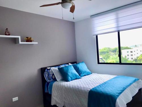 Un dormitorio con una cama con almohadas azules y una ventana en DEPARTAMENTO TOTALMENTE NUEVO, AMOBLADO Y DE LUJO EN TONSUPA, en Tonsupa
