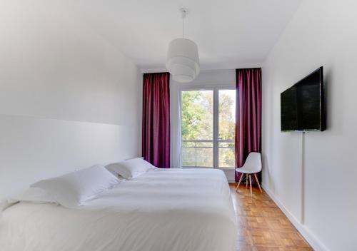 a white bedroom with a large bed and a television at Fauriel Aimé in Saint-Étienne