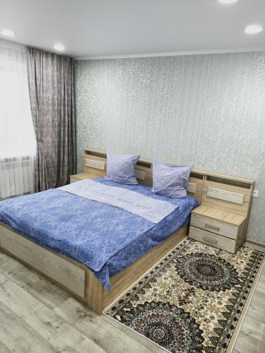 a bedroom with a bed with blue sheets and a rug at ApartLux on Slavskogo 14 in Ustʼ-Kamenogorsk