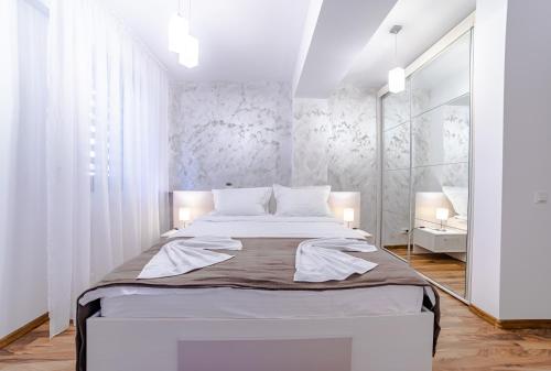 ein weißes Schlafzimmer mit einem großen Bett und einem Spiegel in der Unterkunft MIKRAS LUXURY APARTMENT in Sinaia