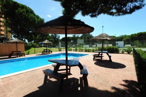 two picnic tables and umbrellas next to a swimming pool at Caparica Sun Centre in Costa da Caparica