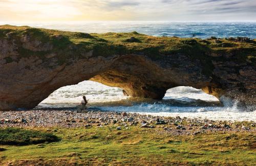 a person standing in front of an arch in the ocean at Deer Lake Horizon Hotel in Deer Lake