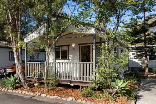 a small white house with a porch and trees at Discovery Parks - Emerald Beach in Emerald Beach