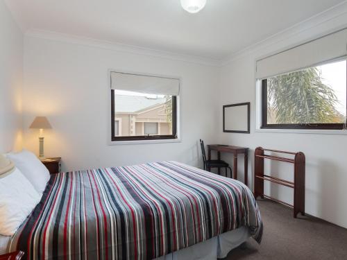 a bedroom with a bed with a striped blanket and two windows at Carindale, 2 19-23 Dowling Street - First floor unit with air con, complex pool and tennis court in Nelson Bay