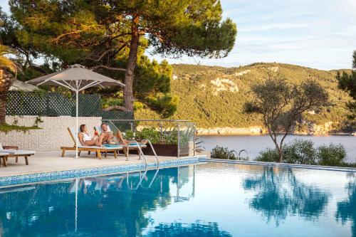 two people sitting in chairs next to a swimming pool at Akrotiri Beach Resort Hotel - Adult Friendly in Paleokastritsa