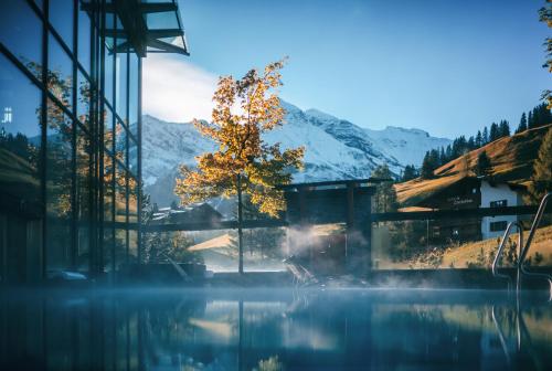 a tree in front of a building with a mountain at Wellnesshotel Warther Hof in Warth am Arlberg