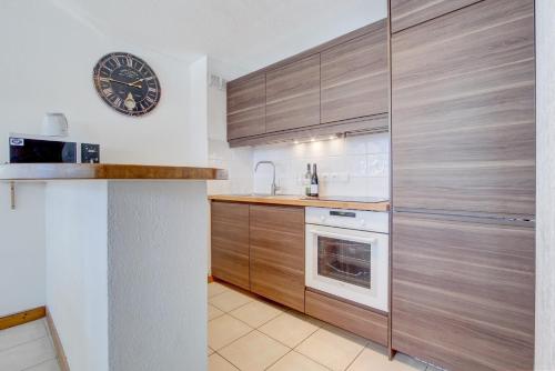 a kitchen with wooden cabinets and a clock on the wall at Slalom Apartment - Very Town Centre - Snow and Trek - Morzine in Morzine