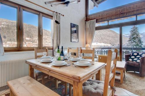 une salle à manger avec une table, des chaises et des fenêtres dans l'établissement Le Pleney Apartment - Snow and Trek, à Morzine
