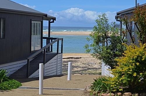 a house on the beach with the ocean in the background at Tuross Beach Cabins & Campsites in Tuross Heads