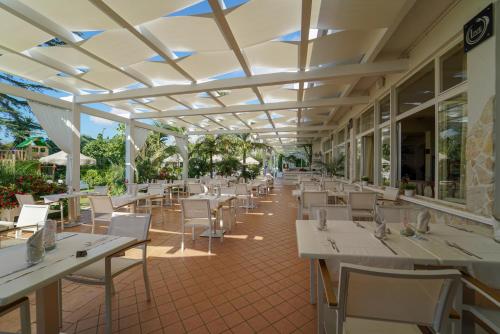 un restaurante con mesas y sillas blancas y ventanas en La Bussola Hotel Calabria, en Capo Vaticano
