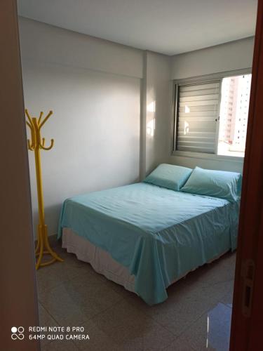 a bedroom with a bed with blue sheets and a window at Apartamento setor bueno in Goiânia