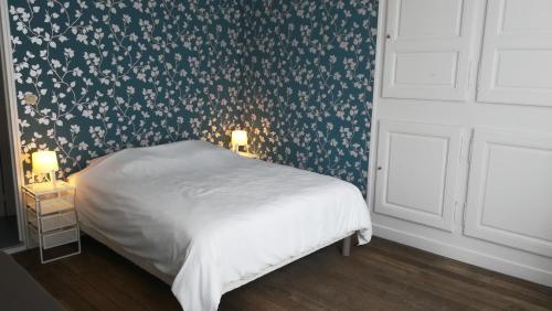 a bedroom with a white bed with a floral wallpaper at Le Logis des Dames in Sedan