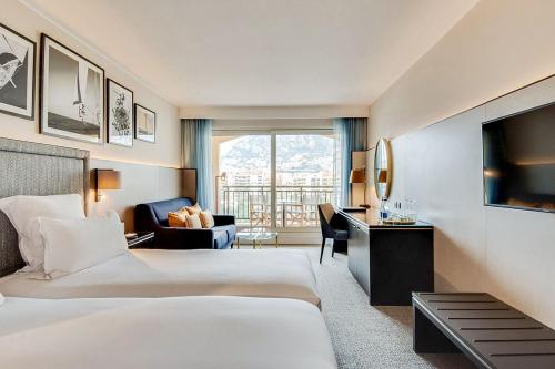 a hotel room with two beds and a desk at Hôtel Columbus Monte Carlo in Monte Carlo