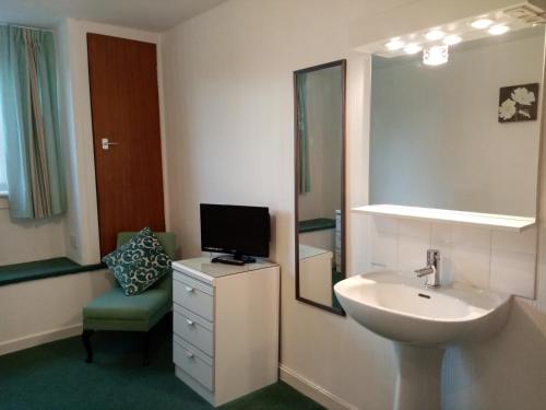 a bathroom with a sink and a tv and a chair at The Laurels Guest House in Blairgowrie