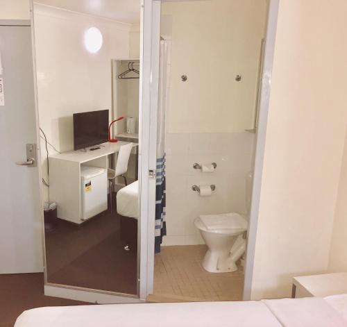 a bathroom with a toilet and a desk with a television at Turbot House Hotel in Brisbane