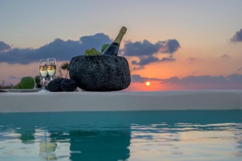 a bowl of fruit and wine glasses on the edge of a pool at Santolia Art Suites in Oia