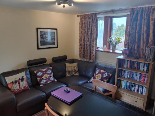 a living room with a black leather couch and a book shelf at Pellcroft Cottage in Holmfirth