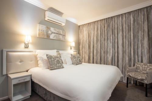 a bedroom with a large white bed and a chair at Devonvale Golf & Wine Estate in Stellenbosch