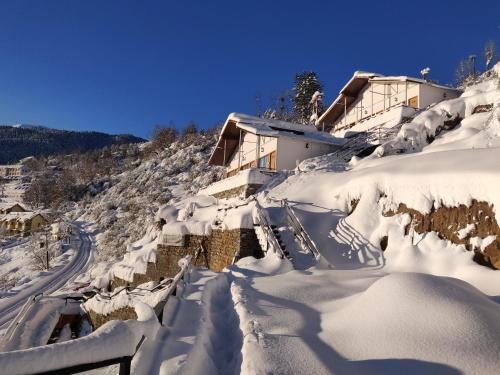 a house covered in snow next to a road at Mountain Rover Auli Resort in Joshīmath