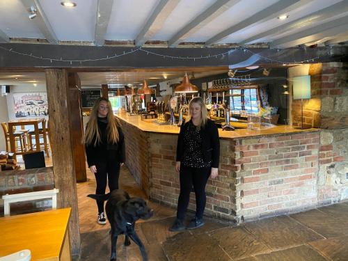 two women standing in front of a bar with a dog at The Bat & Ball Cuddesdon in Oxford