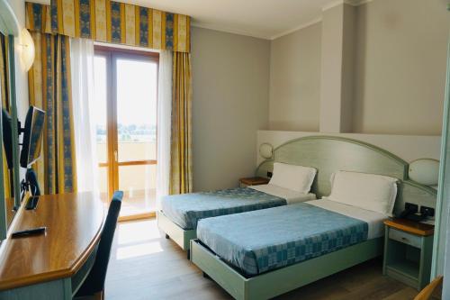 a hotel room with two beds and a desk and a window at Hotel Europa Milano in Rosate
