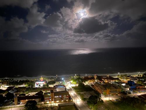 a city at night with the moon over the ocean at Flat PontaNegra Paradise in Natal