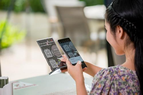 a woman sitting at a table looking at her cell phone at Altera Hotel and Residence by At Mind in Pattaya Central