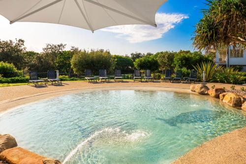 a large swimming pool with an umbrella and chairs at Mantra on Salt Beach in Kingscliff