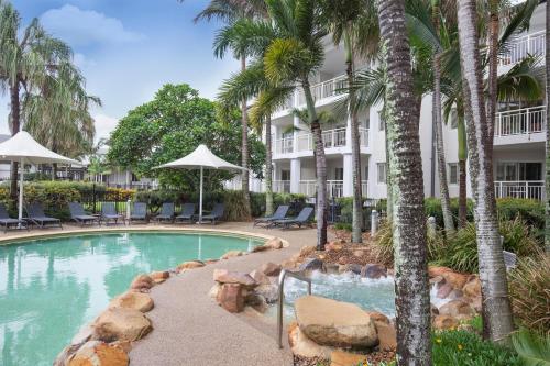 a swimming pool with palm trees and a building at Mantra on Salt Beach in Kingscliff