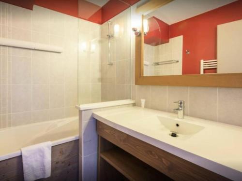 een badkamer met een wastafel, een bad en een spiegel bij Residence Le Christiana - maeva Home in La Tania