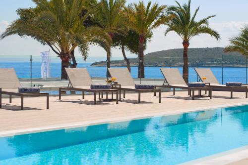 a swimming pool with chaise lounge chairs and palm trees at Meliá Calviá Beach in Magaluf