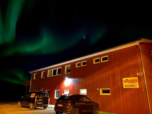 two cars parked in front of a building under the aurora at Midnattsol rom og hytter in Bleik