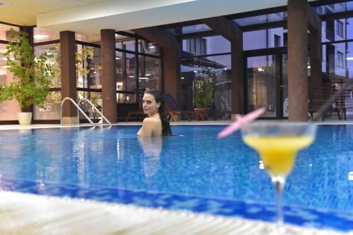 Royal Bansko - Half Board Plus & All Inclusive - Hot Pool & Jacuzzis في بانسكو: وجود امرأة في مسبح مع مشروب