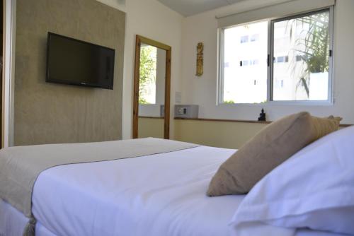 a bedroom with a white bed with a flat screen tv at TAS D VIAJE Suites - Hostel Boutique in Punta del Este